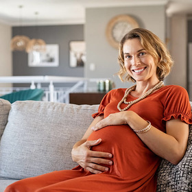 Schwangere sitzt lächelnd auf der Couch