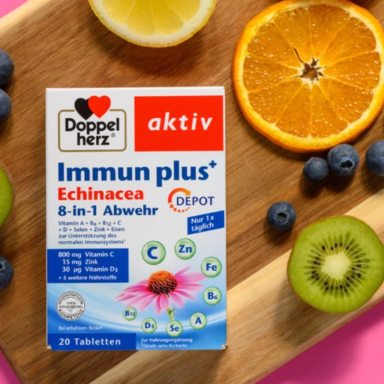 Cutia de pastile "Immun Plus+" de la Doppelherz, evidențiată pe un fundal cu fructe proaspete, cum ar fi portocale, kiwi și afine. Produsul conține vitamina C, zinc, și echinacea, destinat susținerii sistemului imunitar. Informațiile principale sunt prezentate pe ambalaj într-un design clar.