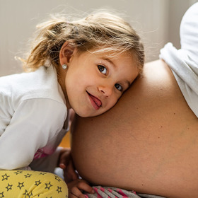 Mädchen legt Kopf auf Bauch der schwangeren Mutter