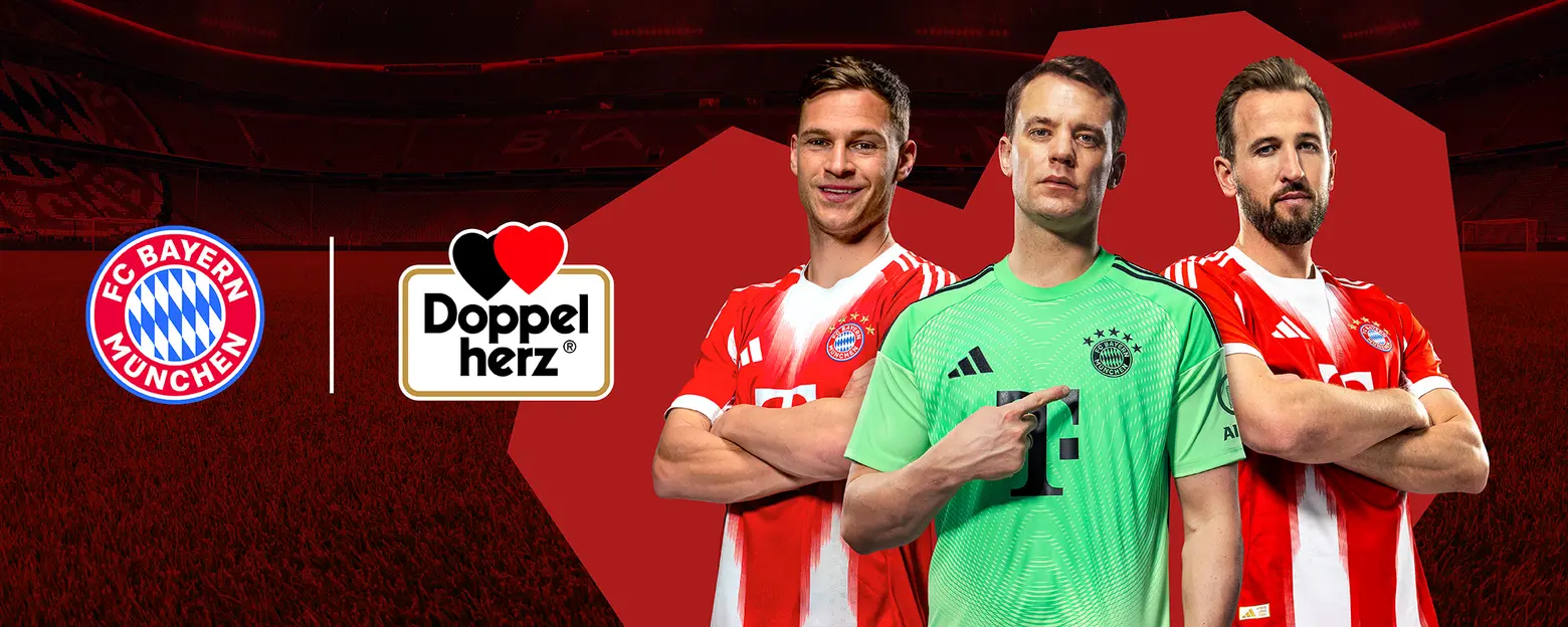 Imaginea prezintă trei jucători de fotbal, îmbrăcați în tricouri roșii și albe ale echipei FC Bayern München. Doi jucători se află în față, iar al treilea este portar, purtând un tricou verde. Logo-ul brandului Doppel Herz este vizibil între ei. Fundalul este un stadion.